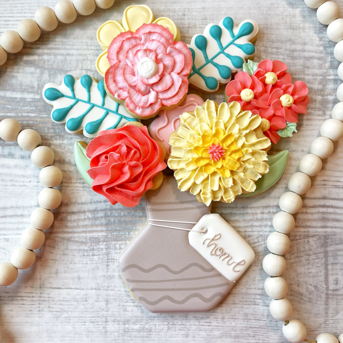 A pastel gray hexagonal cookie vase with wavy stripes holding colorful flower and leaf sugar cookies from the flour box club set