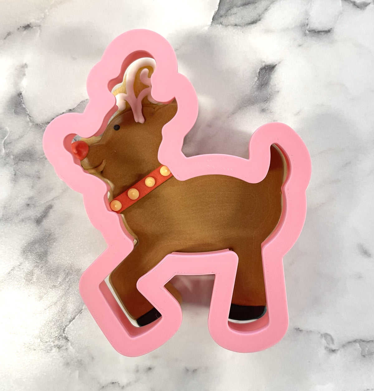 Pink plastic flying reindeer cookie cutter with brown interior red nose and orange collar with yellow dots