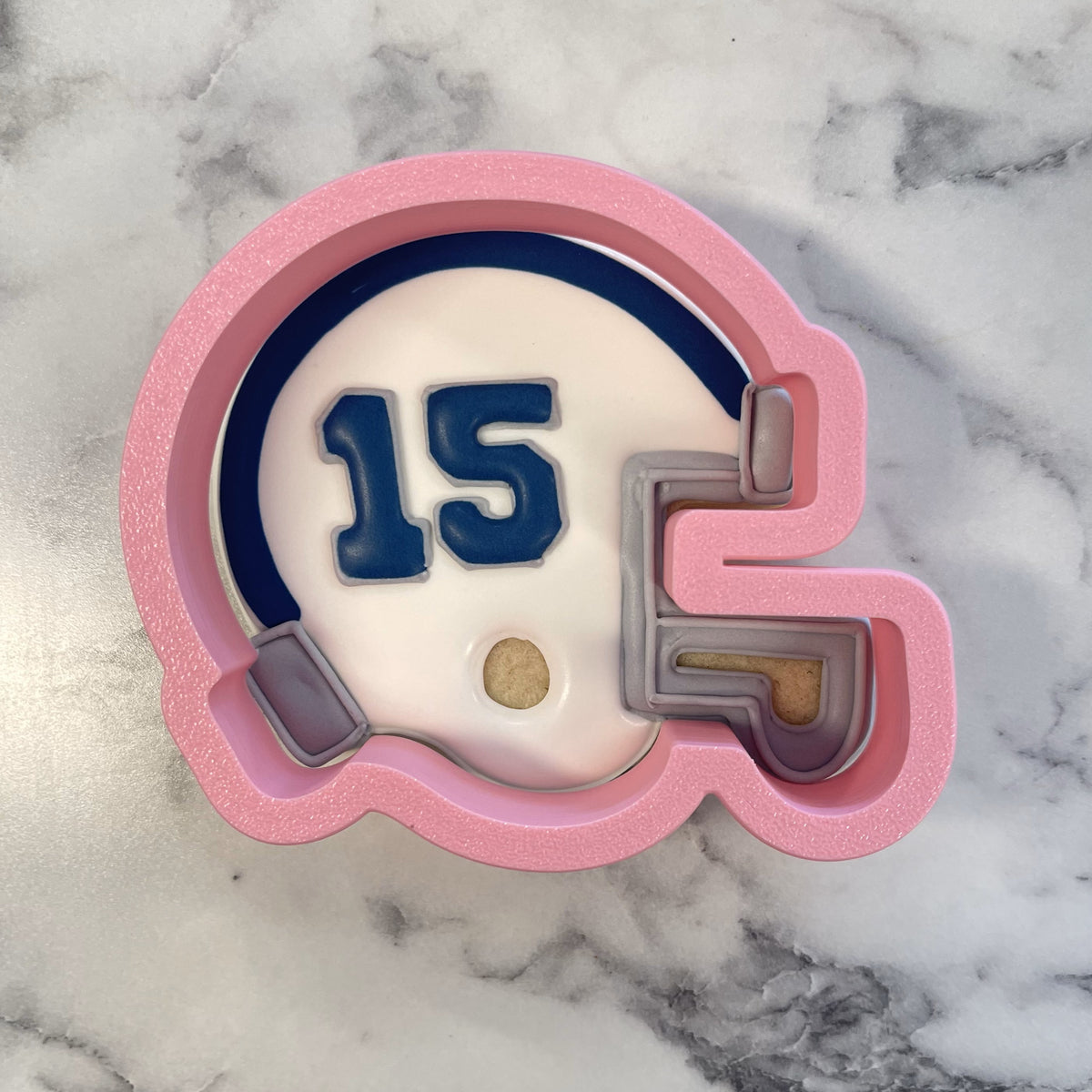 Pink glittery silicone football helmet cookie cutter with navy blue number 15 and gray face mask details