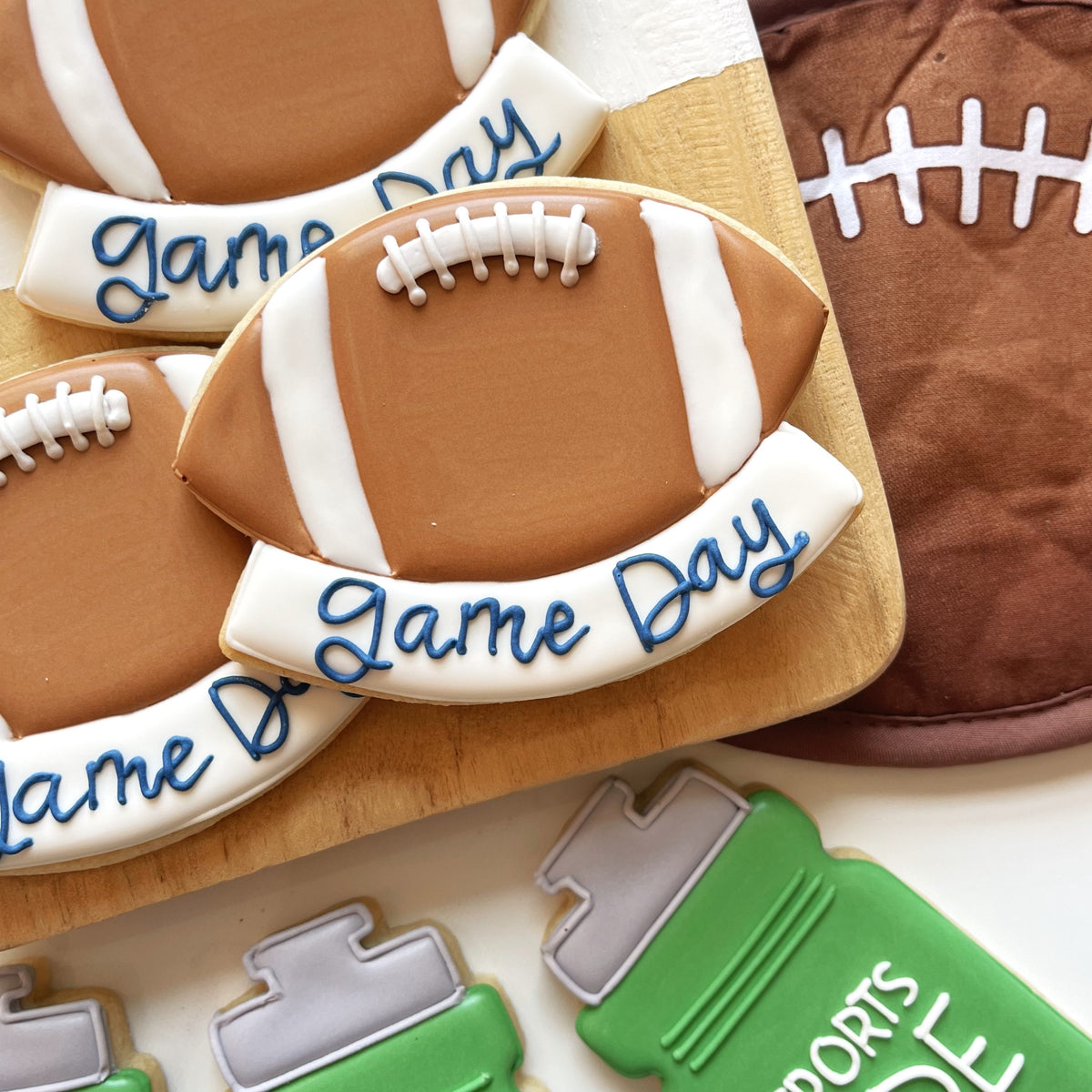Brown football-shaped cookie with white icing stripes and blue game day lettering from football cookie cutter bundle