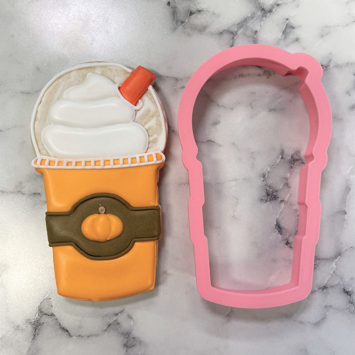 Orange pumpkin spice latte frappuccino cookie cutter with pink silicone material alongside cookie with whipped cream and straw