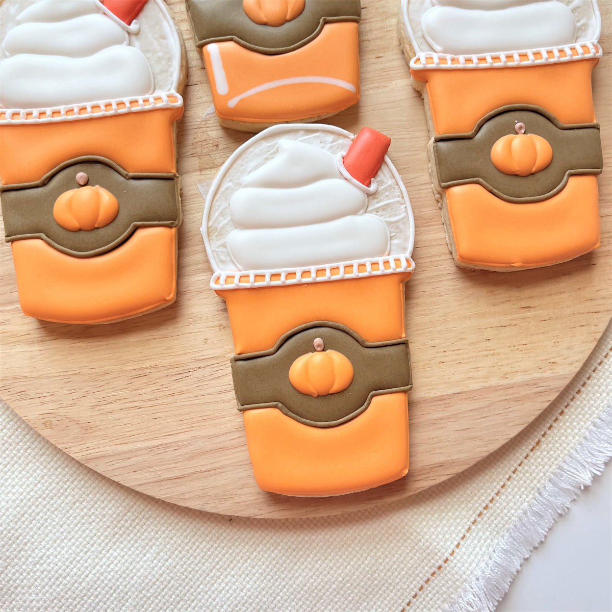 Orange frosted cookie shaped like a pumpkin spice latte with white icing swirls and orange candy straw for frappuccino cutter