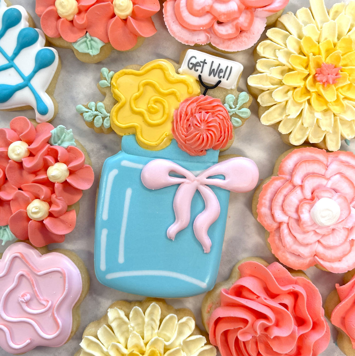 A light blue sugar cookie shaped like a mason jar with yellow and coral frosting flowers and a get well sign