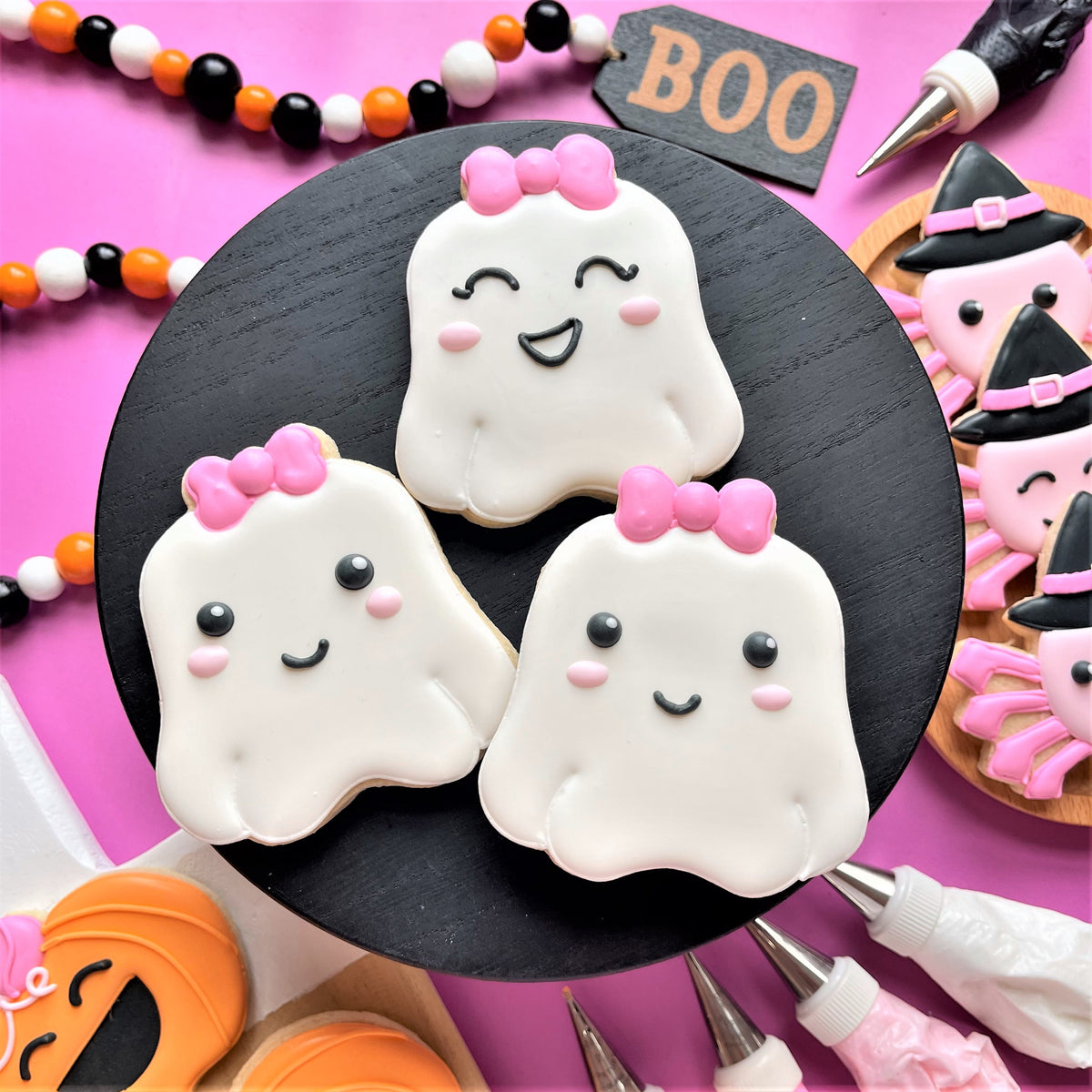 Three white ghost-shaped cookies with pink bows and smiling faces made using the Chubby Ghost Flour Box Club cookie cutter