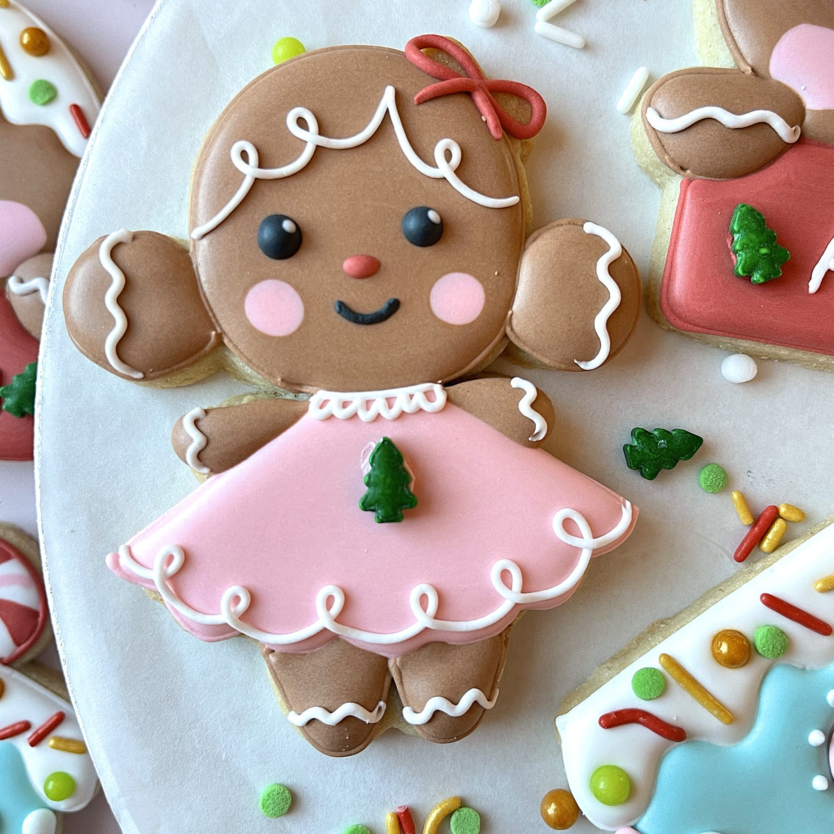 A charming gingerbread girl cookie with pink icing dress white piping and red bow made with a buns cookie cutter
