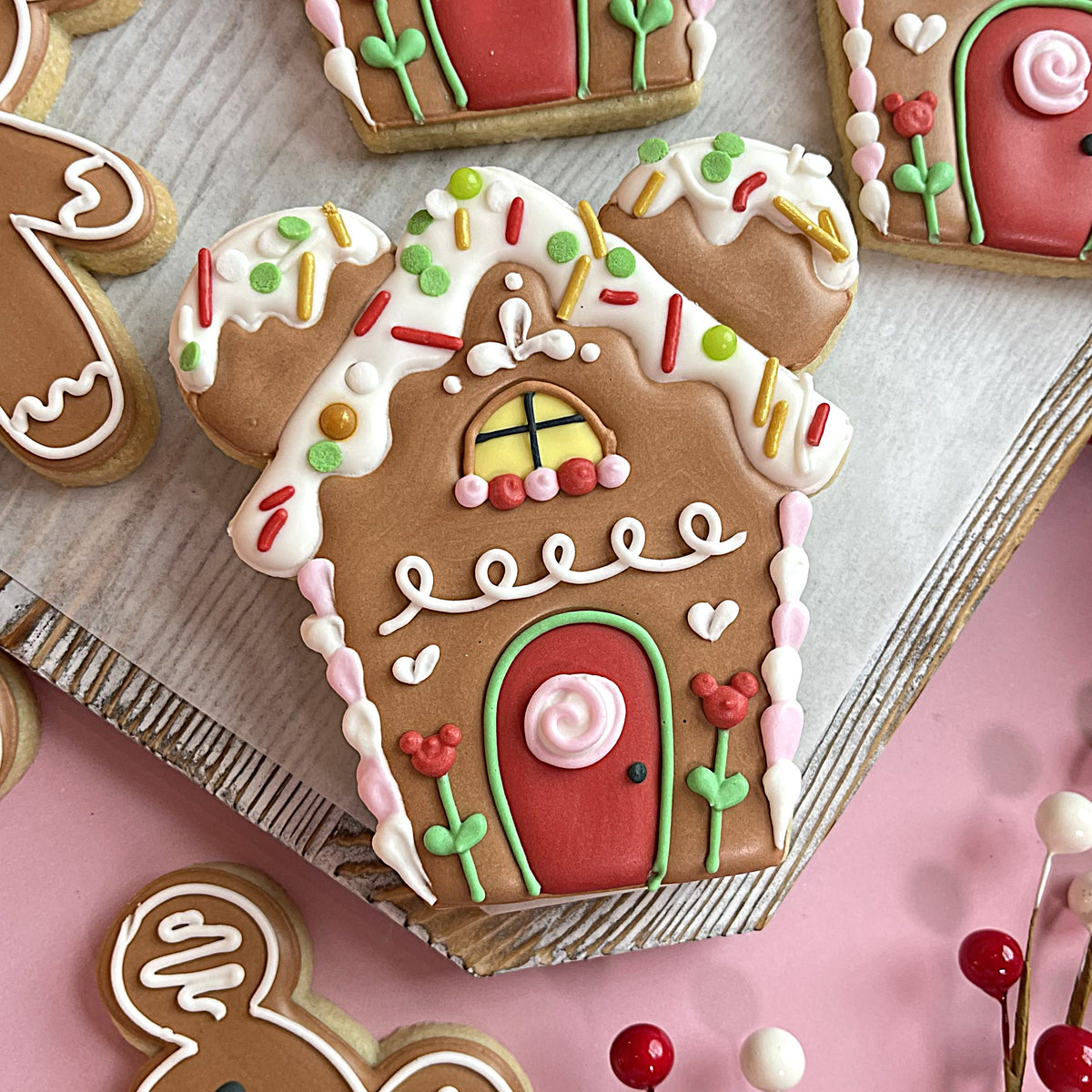 A gingerbread house cookie with brown base red door white icing colorful sprinkles and mickey mouse accents from mouse christmas cookie cutter bundle
