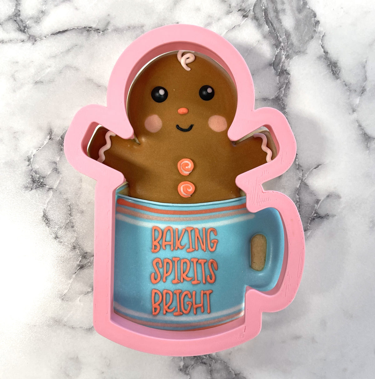 Pink silicone gingerbread man cookie cutter peeking out of blue mug with baking spirits bright text in orange