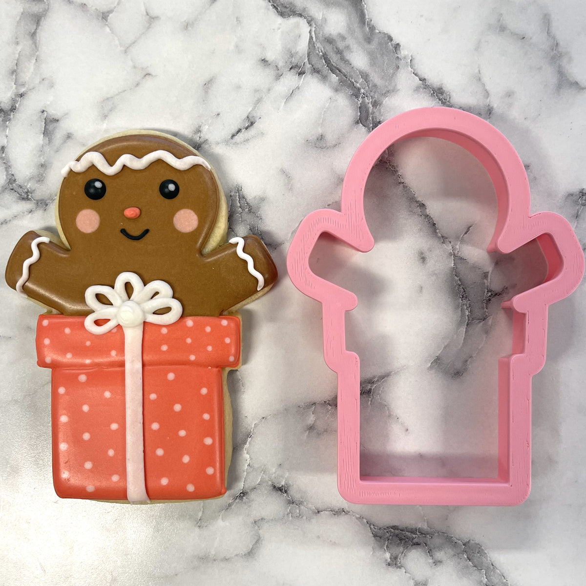 A pink plastic gingerbread man cookie cutter with a gift box design for festive holiday baking
