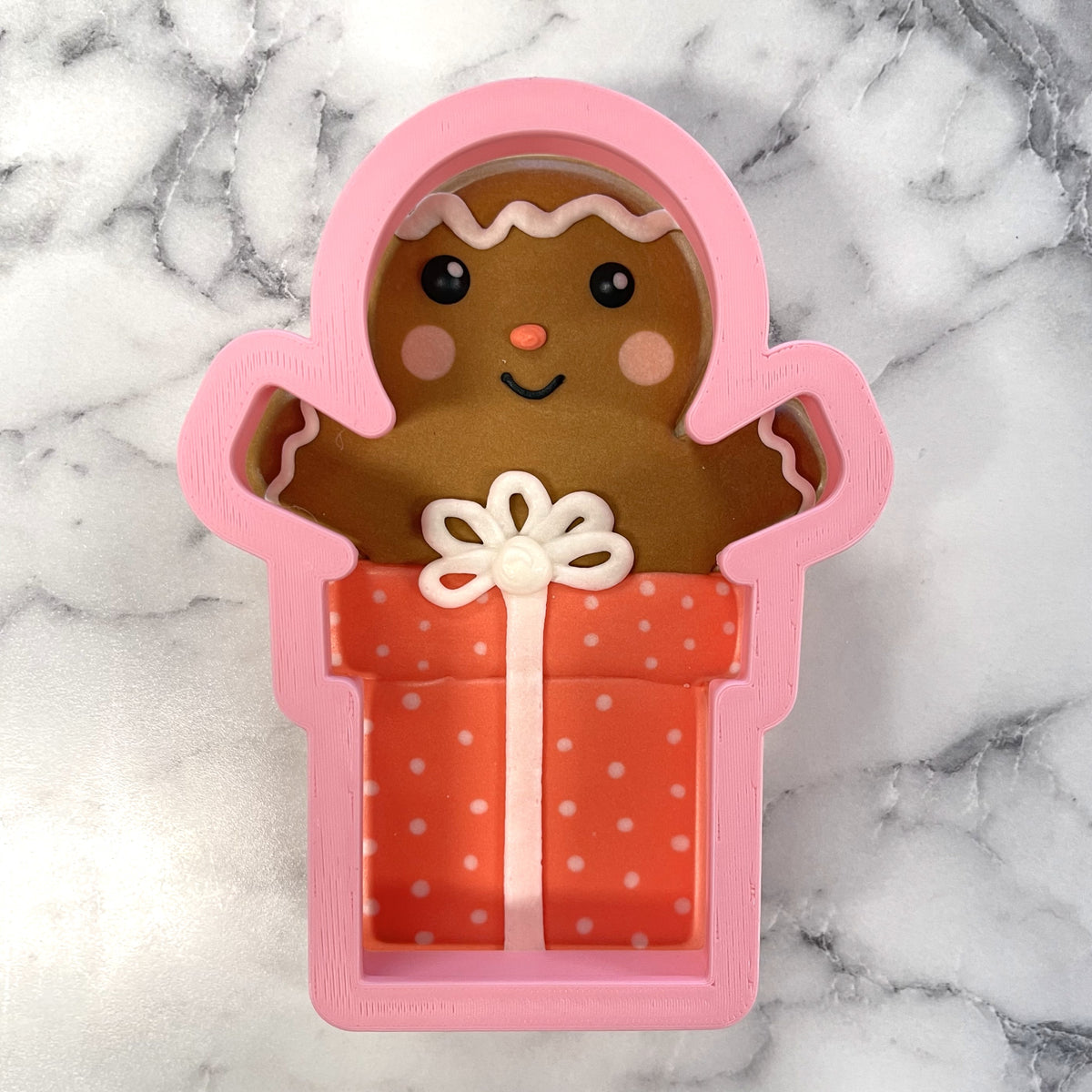 Pink gingerbread man cookie cutter holding an orange polka-dotted gift box with white bow for holiday baking