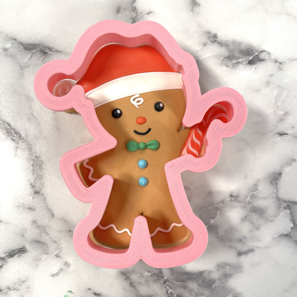 Pink plastic gingerbread with santa hat cookie cutter featuring a red hat green bow tie and blue buttons