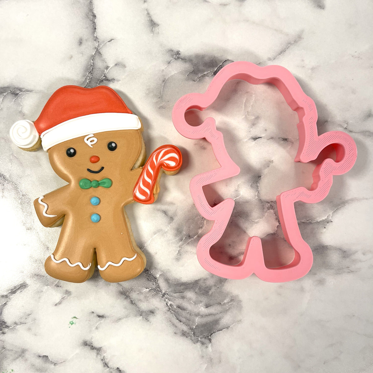 A gingerbread man cookie with a red and white santa hat green bow tie blue buttons and candy cane accessory