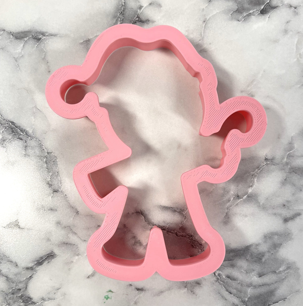 Pink plastic gingerbread cookie cutter shaped like a cartoon character with curly hair and puffy sleeves wearing santa hat