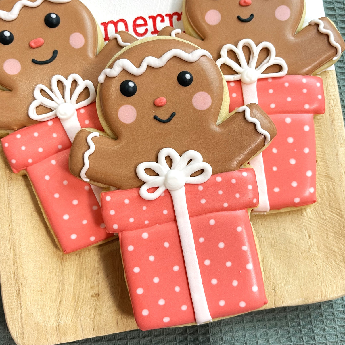 Cute brown gingerbread man cookie with pink cheeks holding coral polka dot gift box in poppin gingerbread cookie cutter bundle