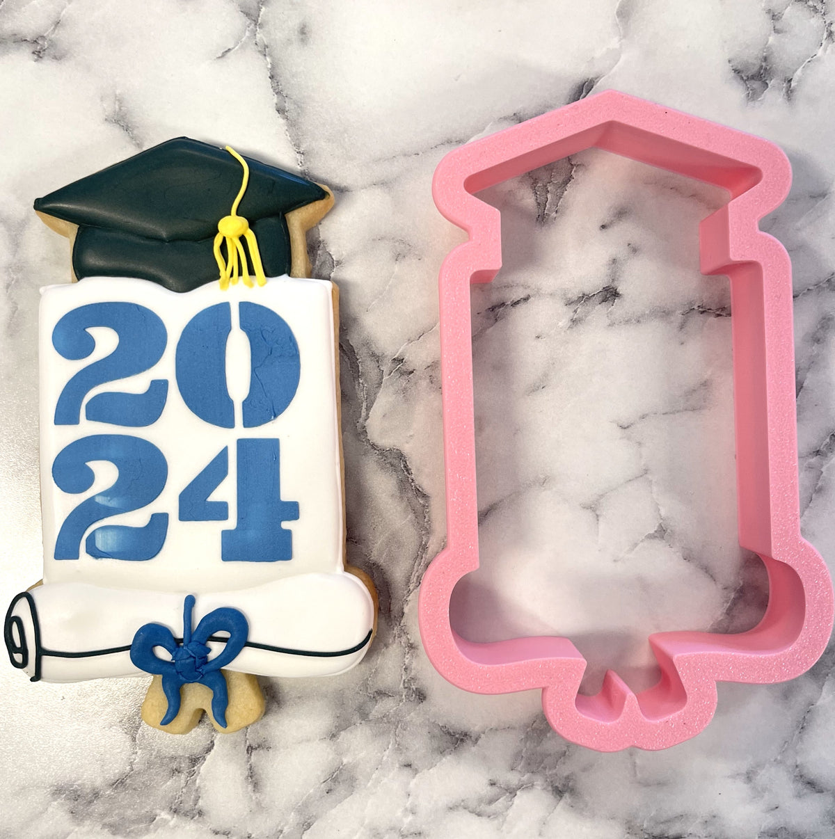A pink plastic graduation-themed diploma scroll cookie cutter with decorative edges and included stencil for yearly plaques