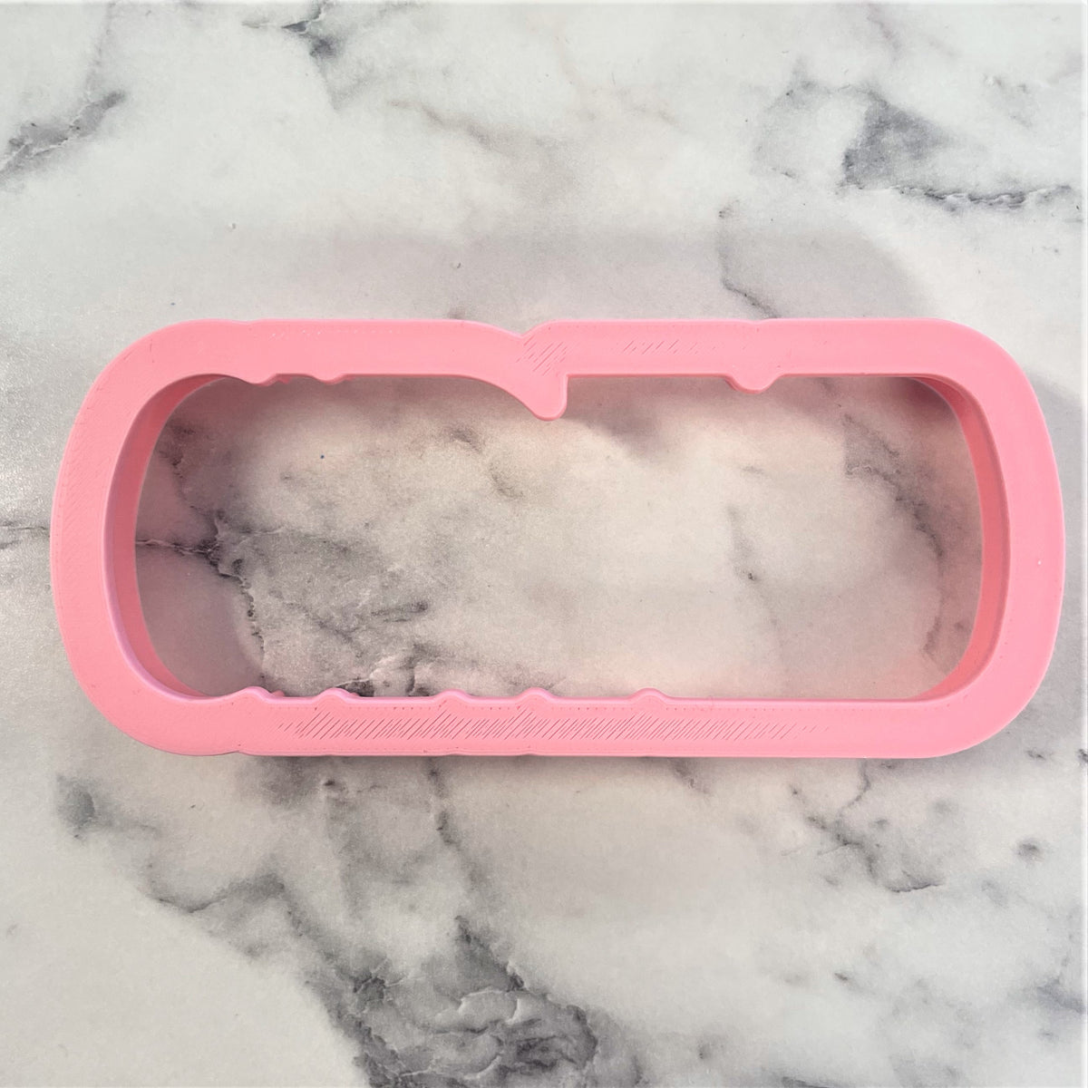 Pink silicone mold shaped like a rectangular phone case with white foamy interior for grad plaque flour box club cookie cutter with stencil