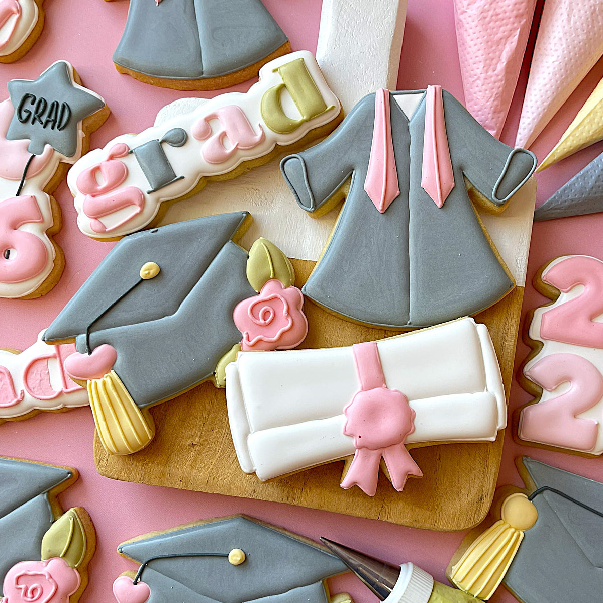 Gray graduation gown cookie with pink satin sash and piped icing from 2026 grad cutter release set