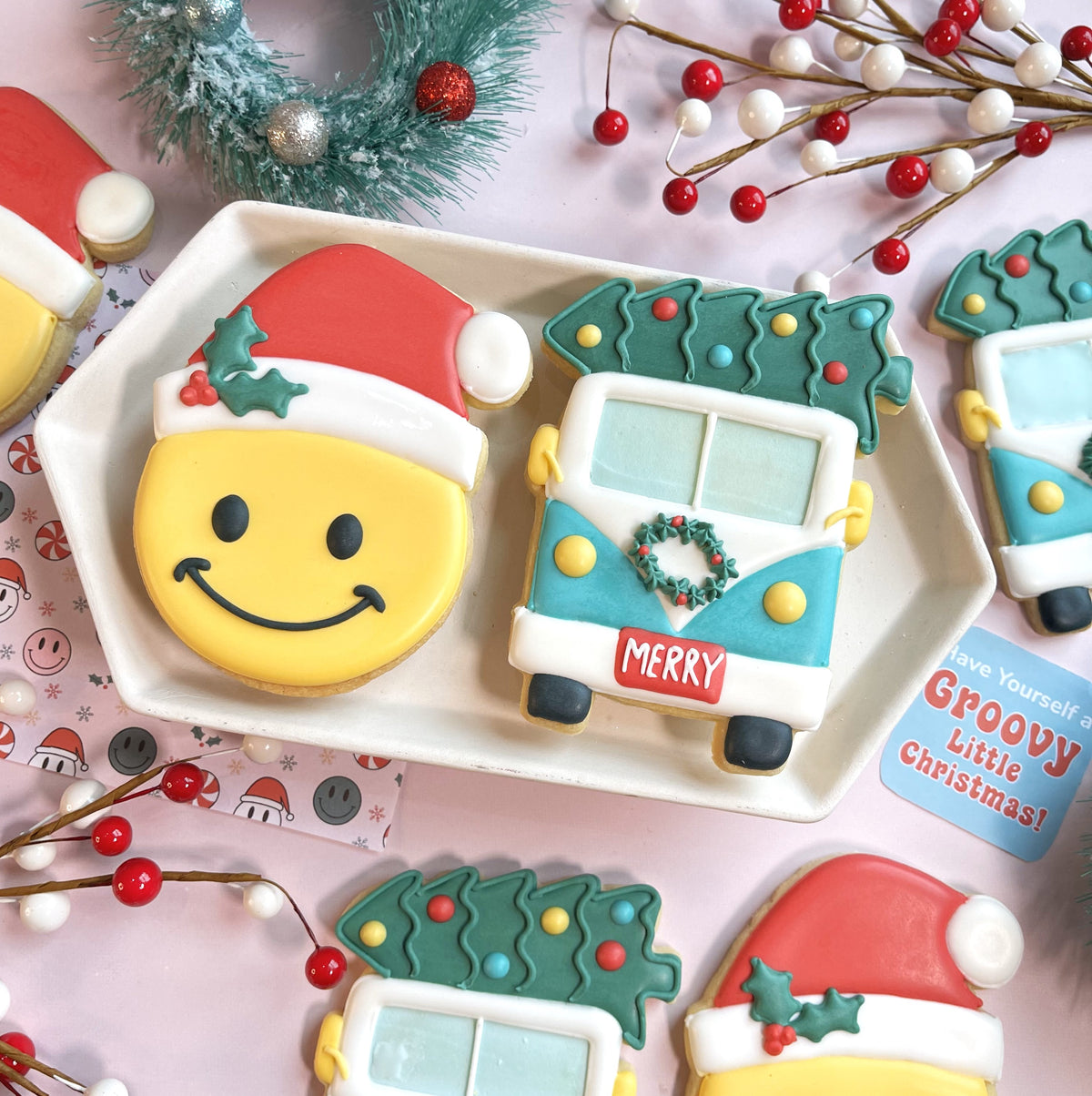 A festive yellow smiley face cookie with a red and white santa hat and green holly made using a bus with tree cookie cutter