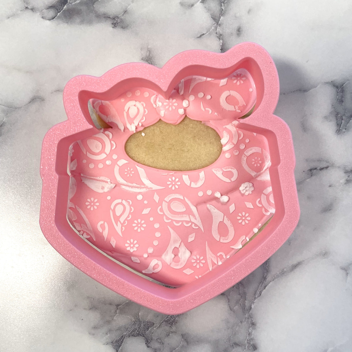 Pink silicone handkerchief cookie cutter shaped like a baby bib with white paisley and floral patterns