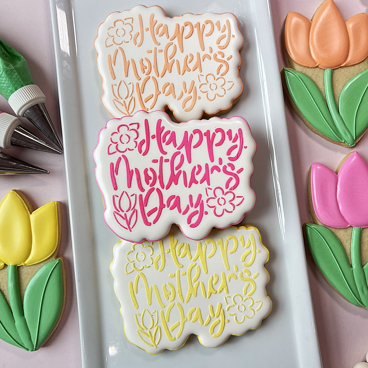 Three happy mothers day floral plaque cookies with white icing colorful script and delicate floral accents made with stencil