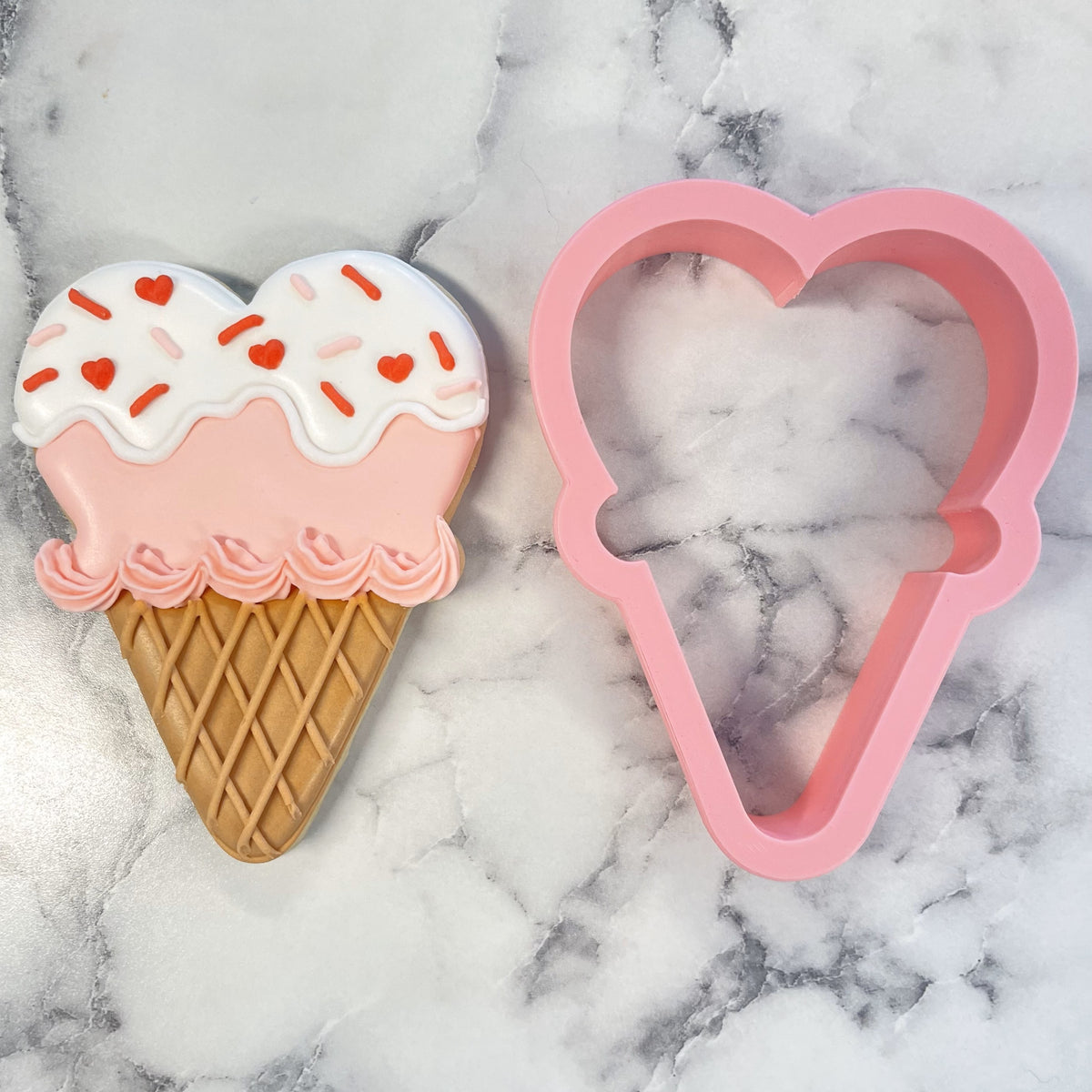 Pink heart-shaped metal cookie cutter next to a decorated heart ice cream cone cookie for baking fun treats