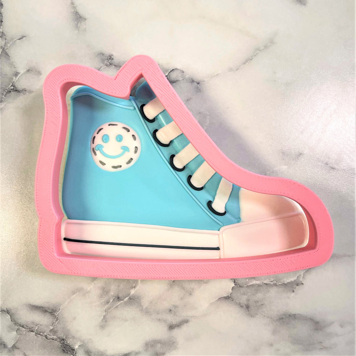 Pink plastic high top sneaker cookie cutter with light blue upper white laces sole and smiling face design