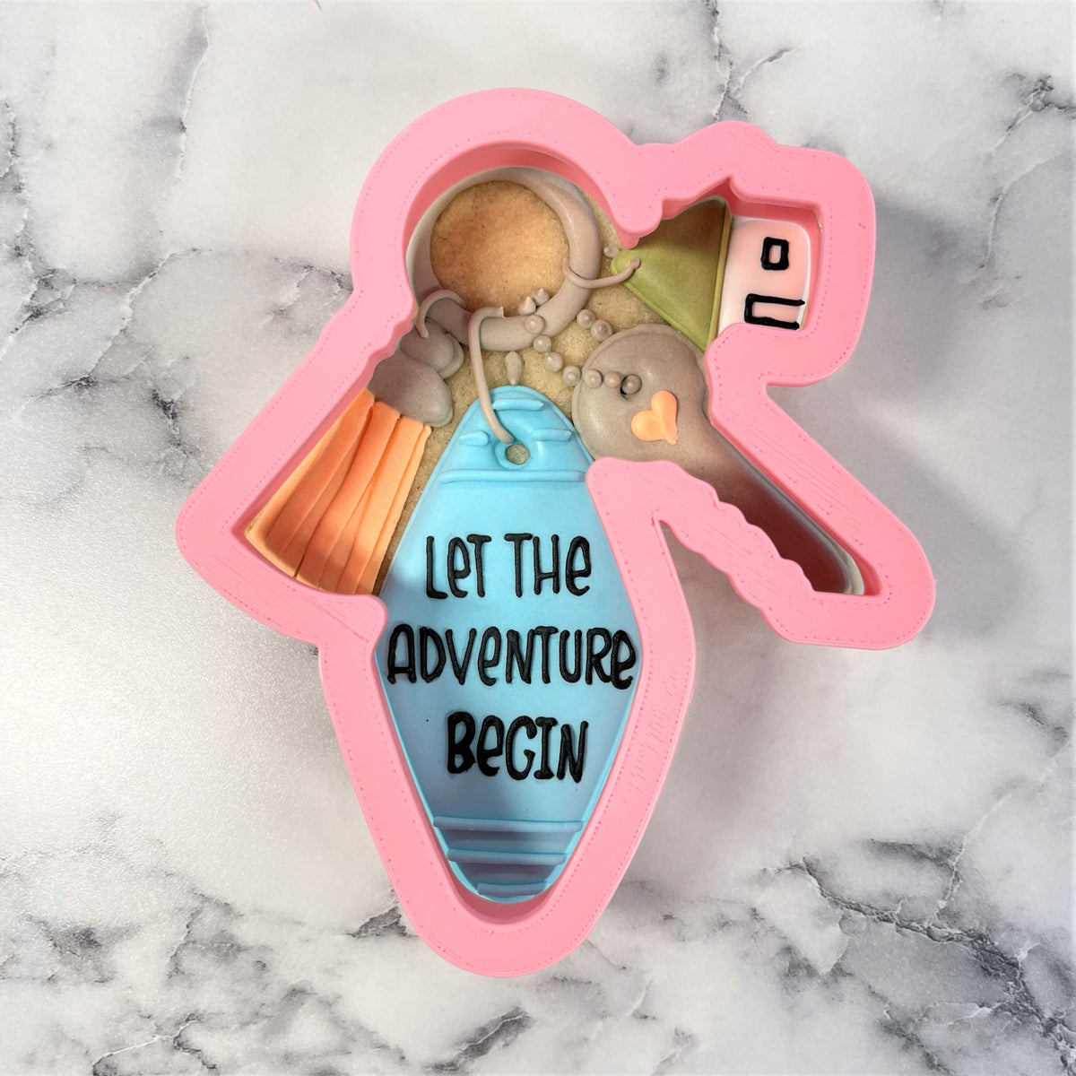 Pink silicone housewarming key ring cookie cutter shaped like a hand holding a keychain with let the adventure begin text