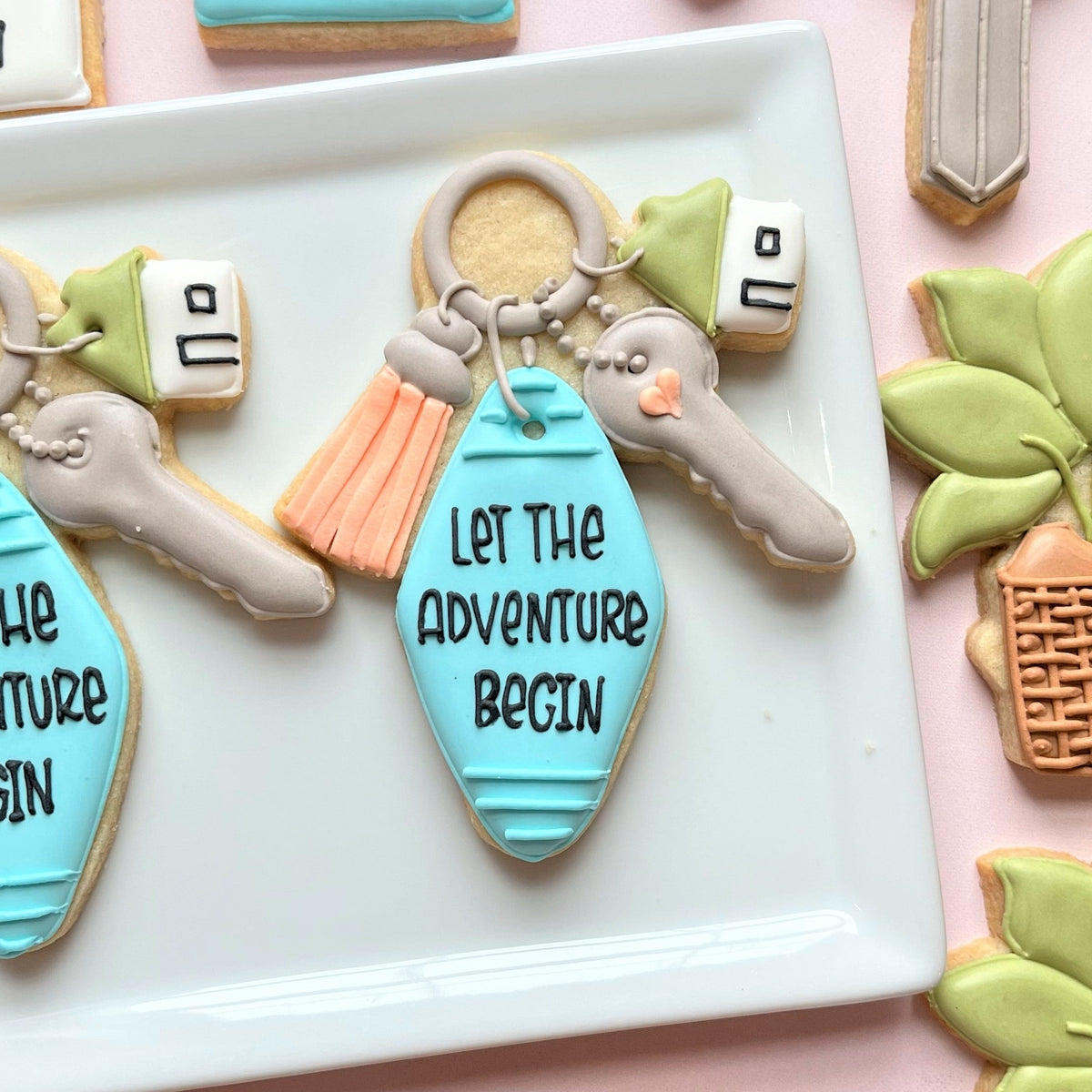 A light blue housewarming key ring cookie cutter shaped like a key with let the adventure begin icing design