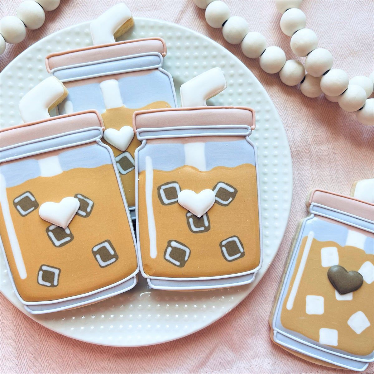 Delicate iced coffee jar-shaped cookies with smooth glossy amber and pastel icing made using iced coffee cup cookie cutter