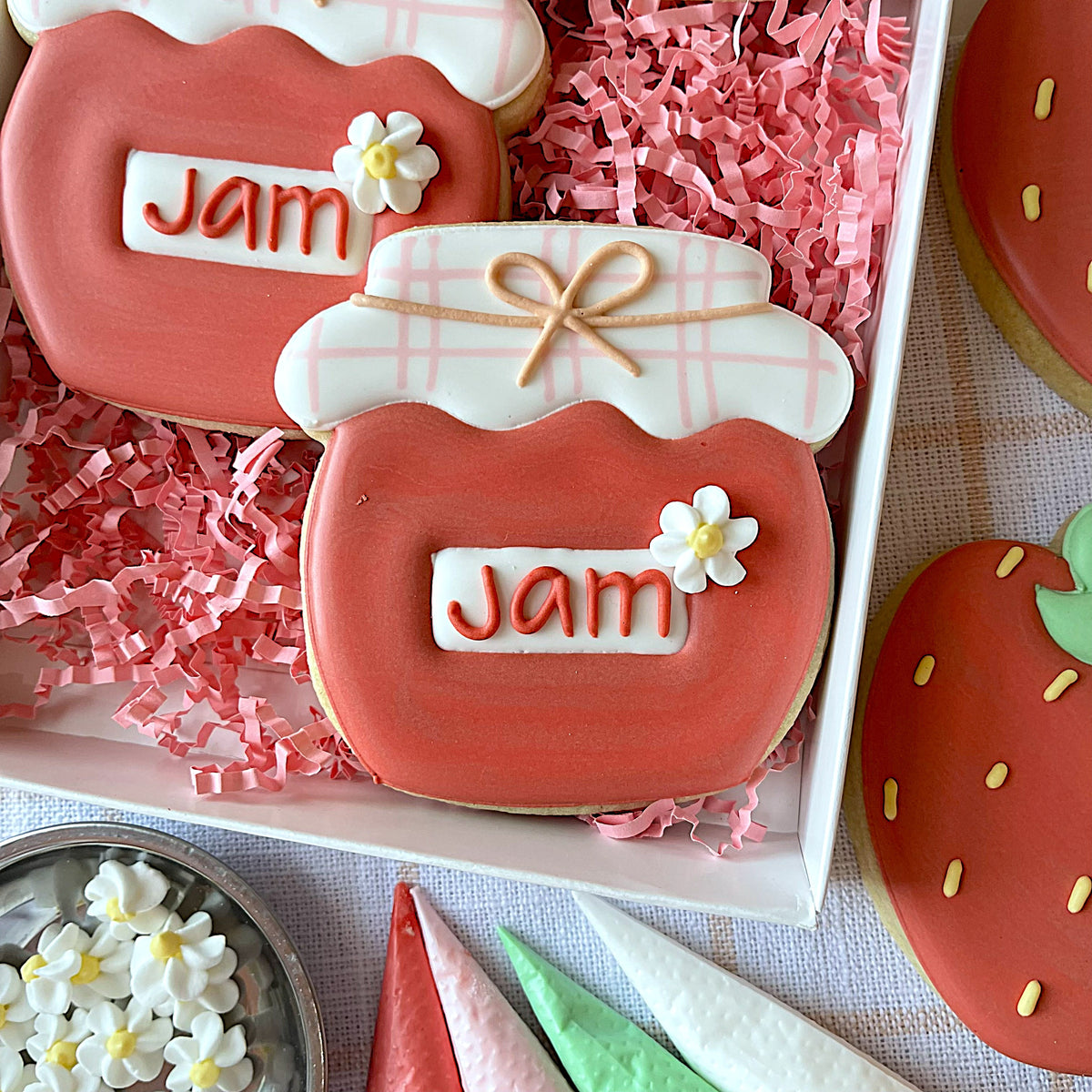 A pink jam jar cookie with white icing lid tan ribbon bow and small white flower made using jam jar cookie cutter