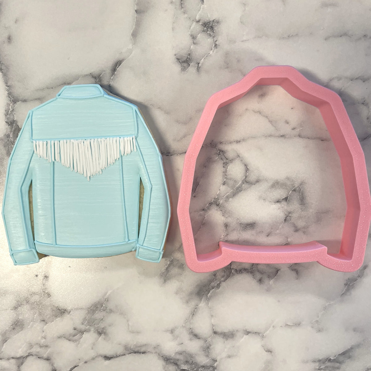 Light blue and pink jean jacket cookie cutters shaped like a fringed jacket for baking and decorating cookies