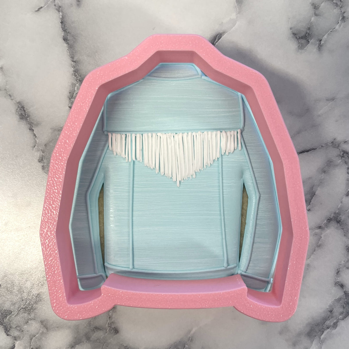 Pink silicone cookie cutter shaped like a light blue jean jacket with white fringe detail for baking and decorating