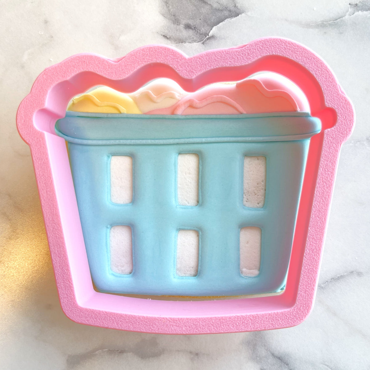 Pink silicone laundry basket cookie cutter mold with light blue interior holding colorful soap bars inside