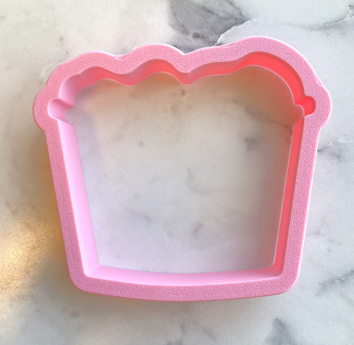 Pink silicone laundry basket cookie cutter with scalloped edges shaped like a cupcake for baking use