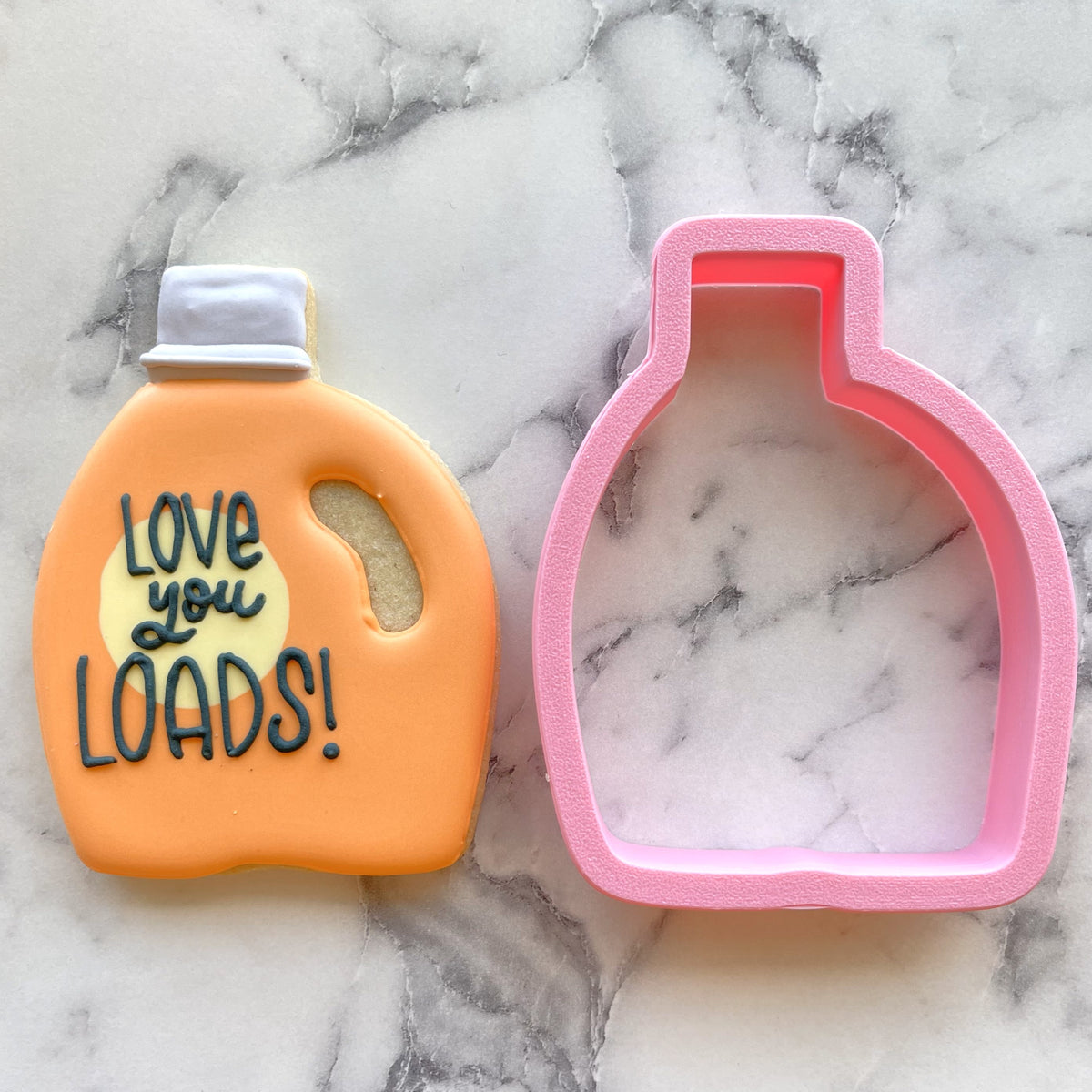 Orange laundry detergent cookie shaped with love you loads in black icing and white lid next to pink silicone mold