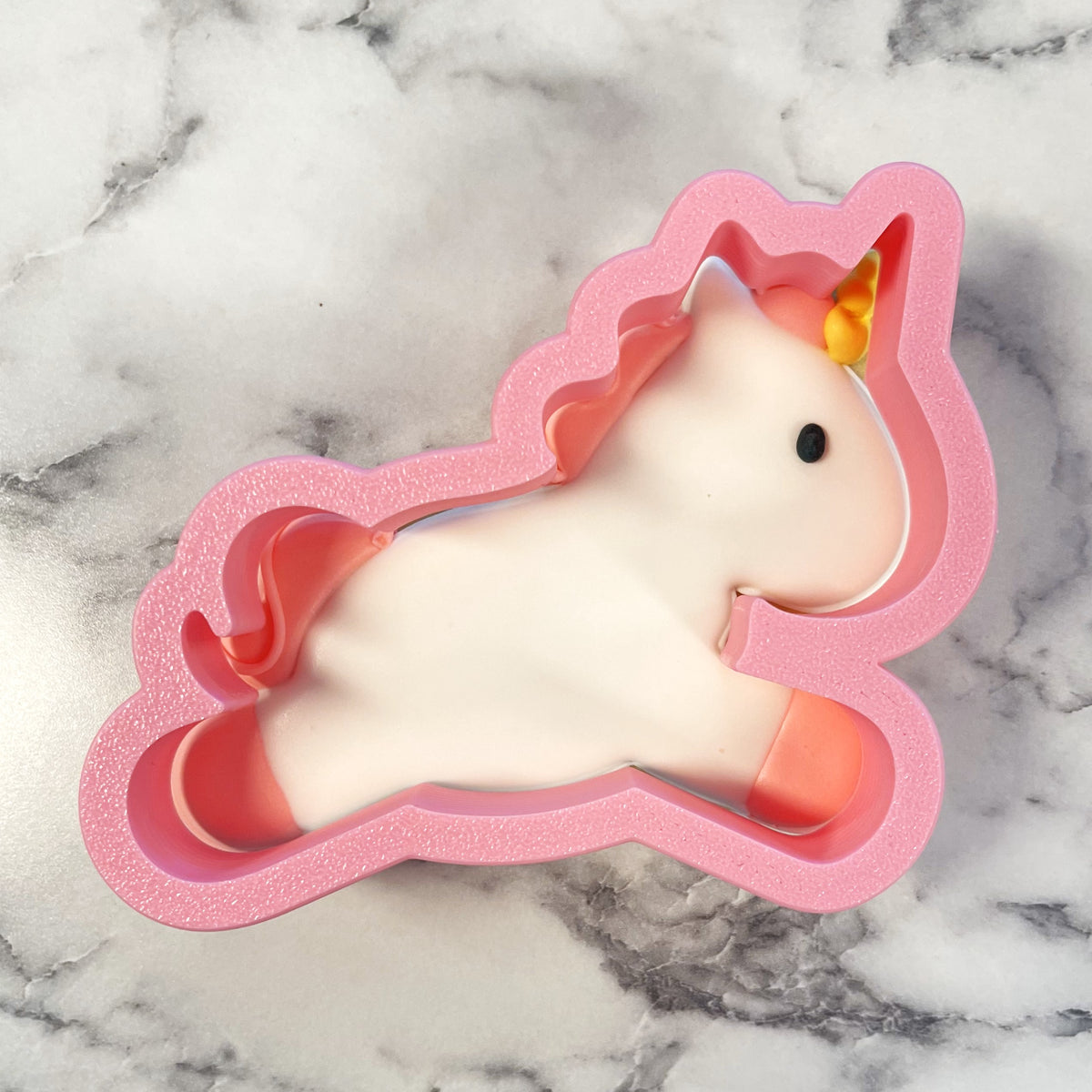 Leaping unicorn cookie cutter with pink glitter, white body, orange mane and tail, yellow horn, and black eye