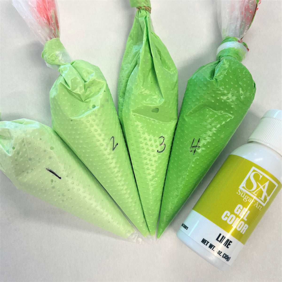 Lime green silicone pastry bags with perforated texture and numbered markings next to lime the sugar art gel color bottle