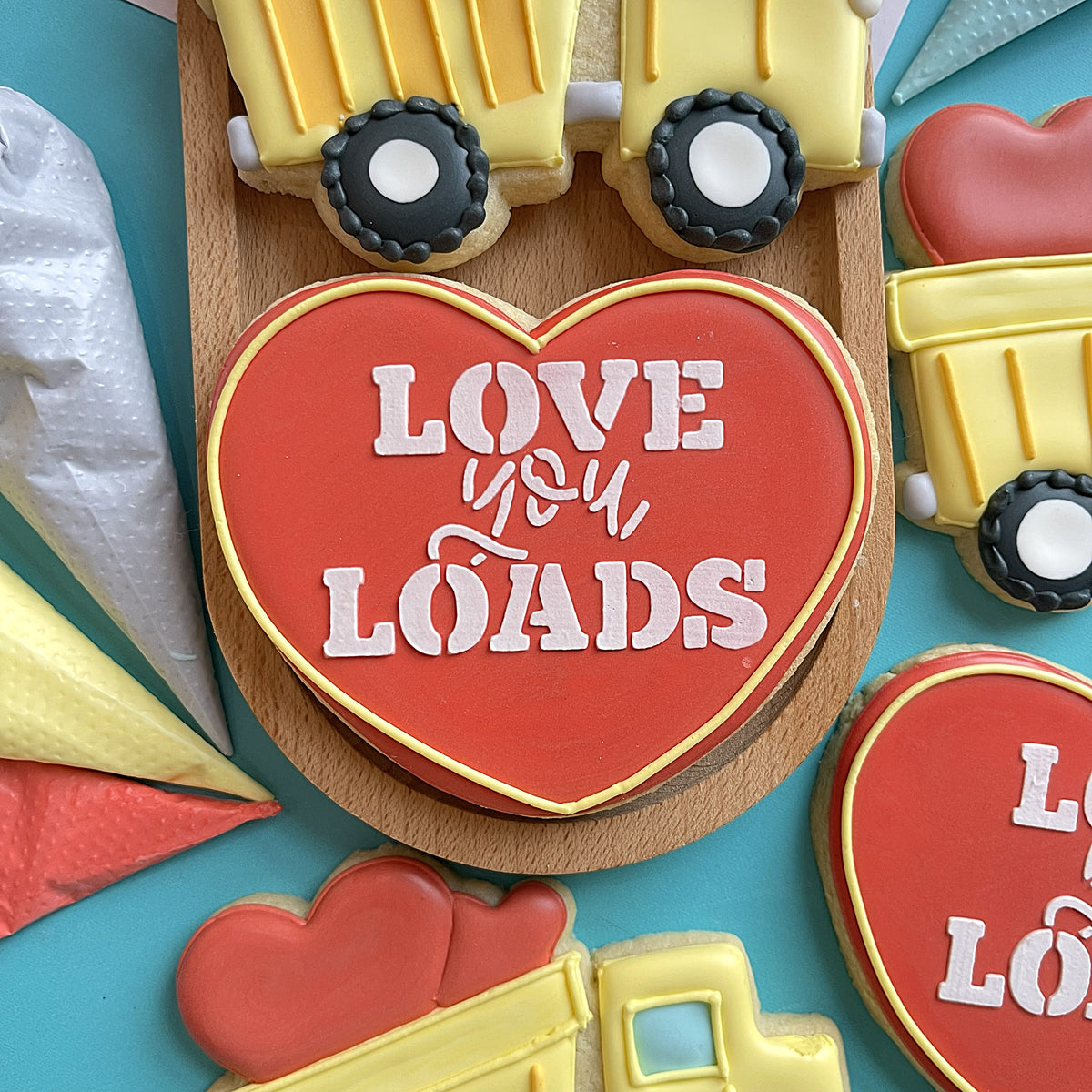 Red heart-shaped cookie with white icing lettering love you loads and yellow border for love you loads stencil
