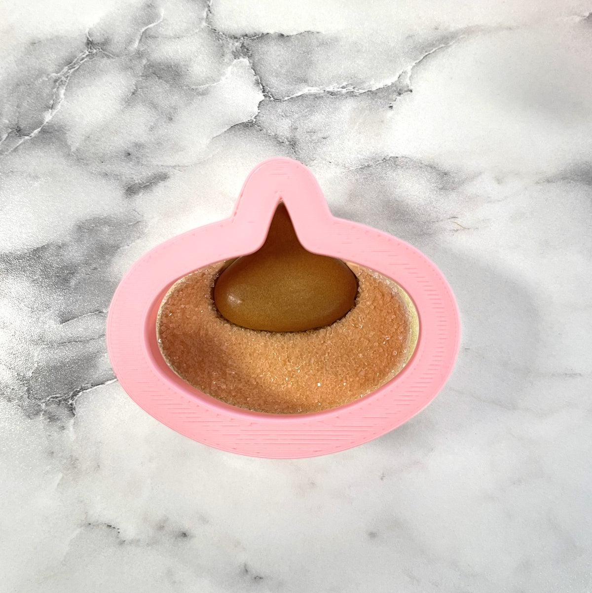 Pink silicone mini pb blossom cookie cutter with a brown glossy candy inside resembling a hersheys kiss candy