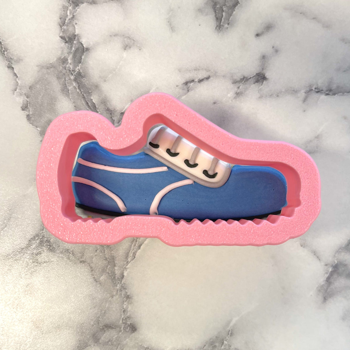 Mini golf shoes cookie cutter in blue and white metal inside pink foam mold for baking and crafting use