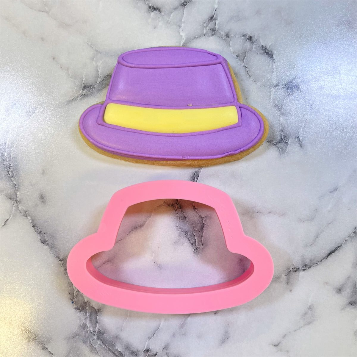 A purple and yellow fedora-shaped cookie with smooth glossy icing made using a mini hat cookie cutter