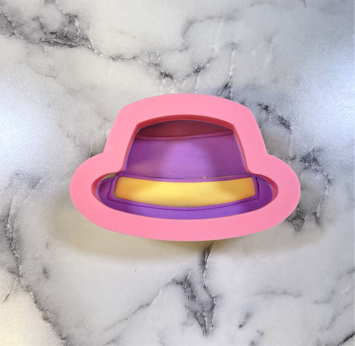 Mini hat cookie cutter made of pink silicone with a purple interior and yellow band detail for baking