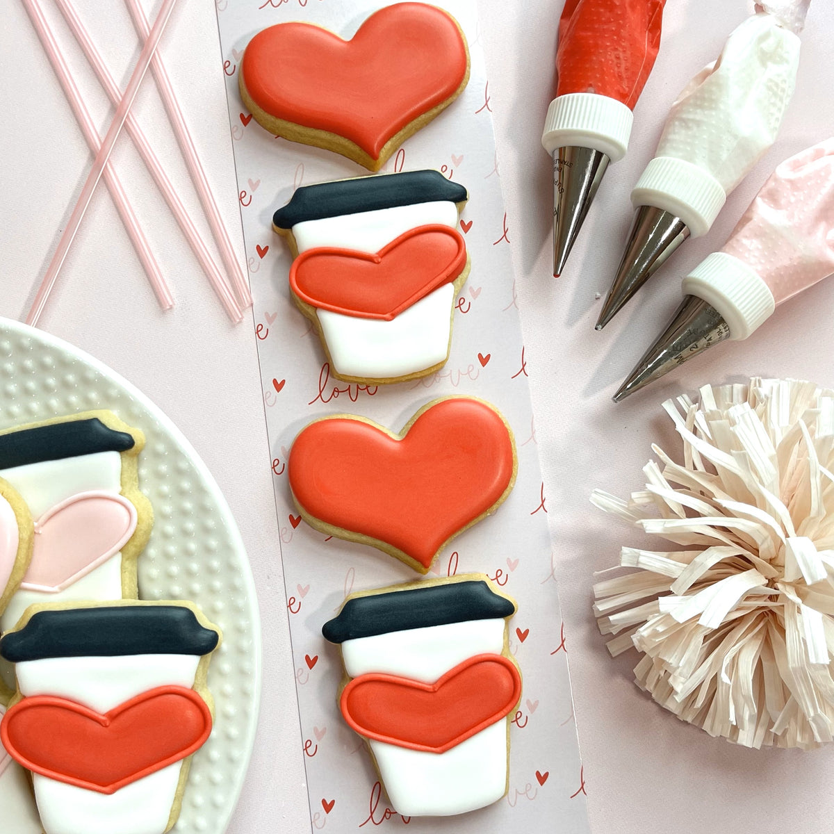 Mini latte heart cookie cutter shaped red cookies with white and black icing on decorative paper sheet