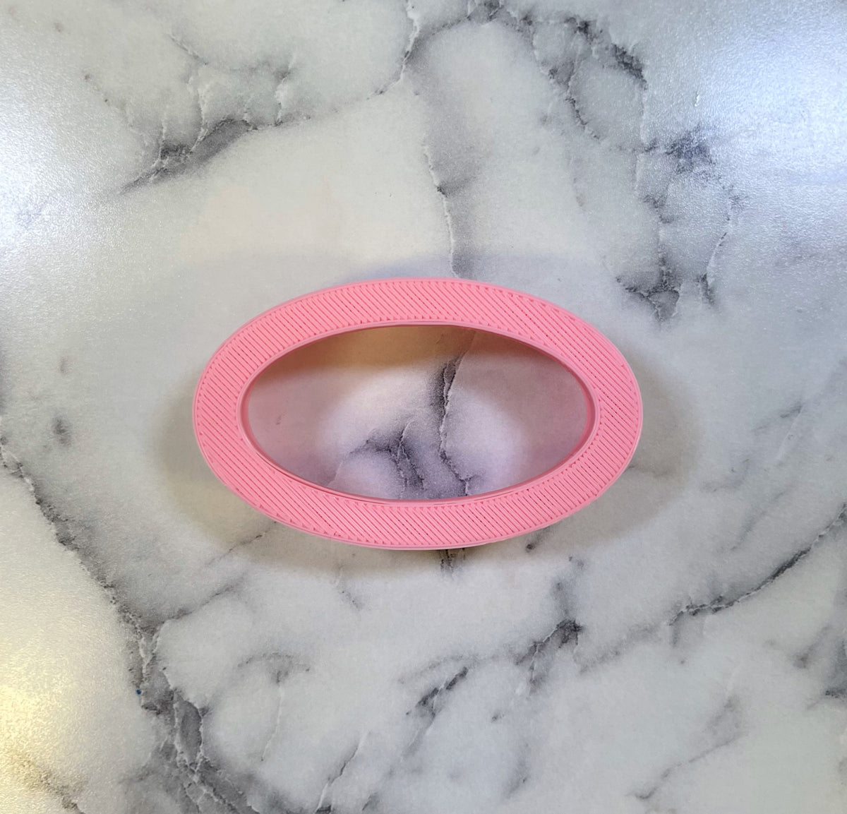 Mini oval cookie cutter in pink silicone with textured ribbed edge for easy grip and precise cutting