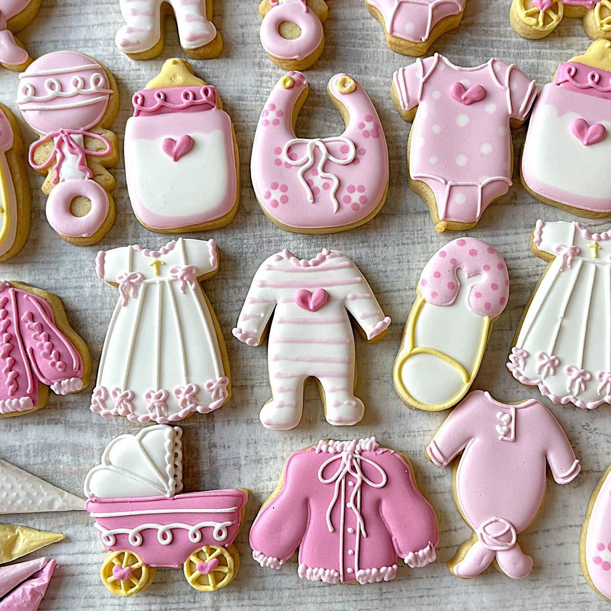 Mini baby cookie cutter bundle with 10 pink and white frosted baby-themed sugar cookies shaped like outfits and bottles