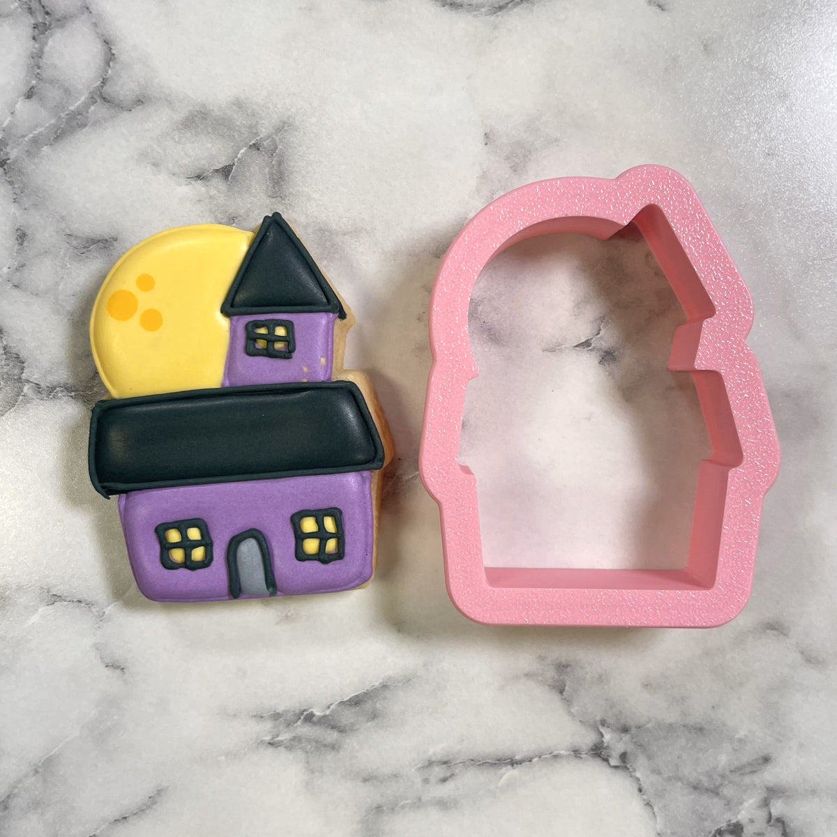 Mini cute chubby haunted house cookie cutter with pink glittery silicone and purple cookie with black roof and yellow windows