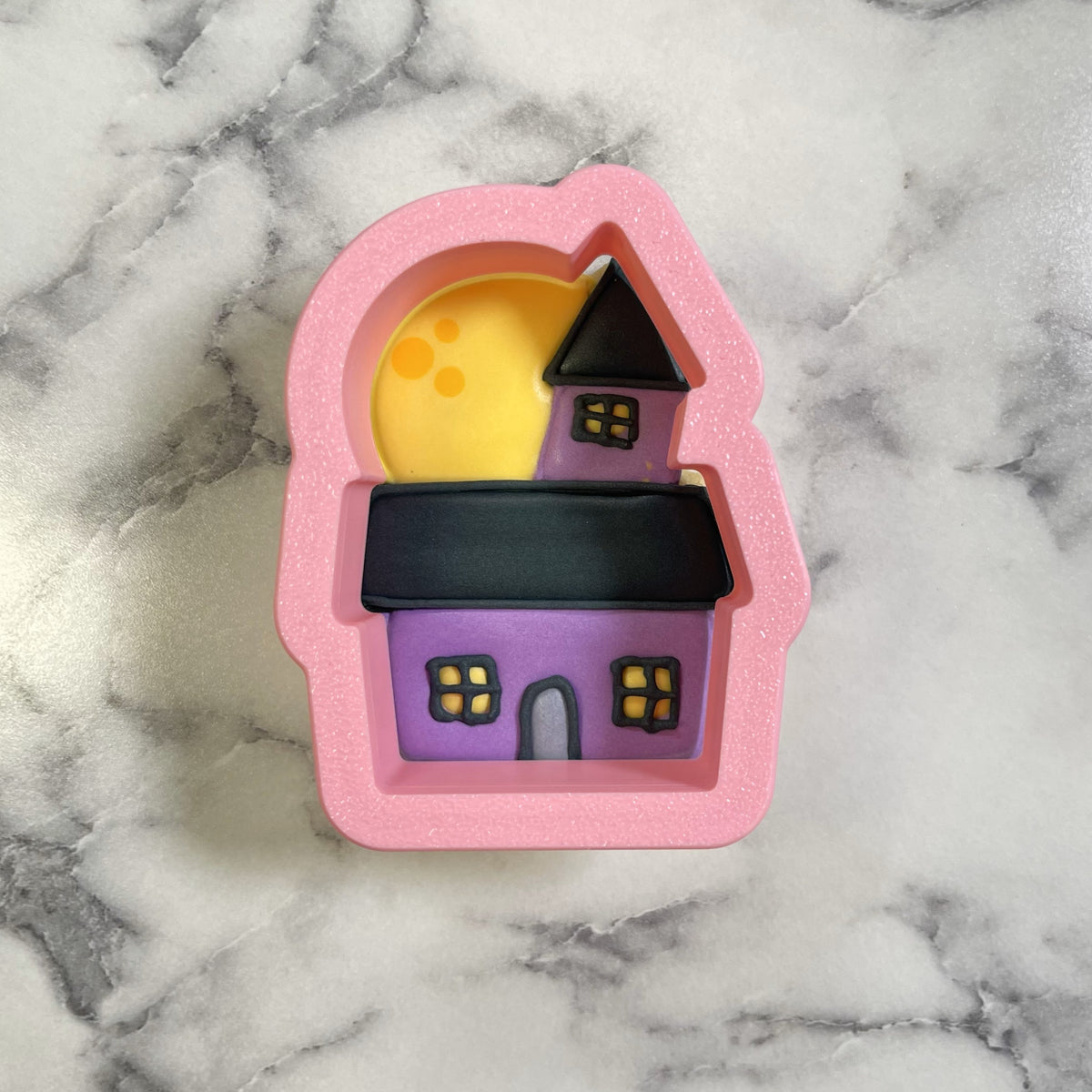 Mini cute chubby haunted house cookie cutter made of pink silicone with purple and black castle design and yellow moon backdrop