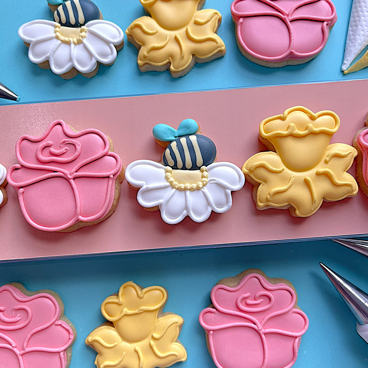 A delicately decorated white daisy cookie with piped icing and a blue and black striped bee in a mini flower cookie cutter bundle
