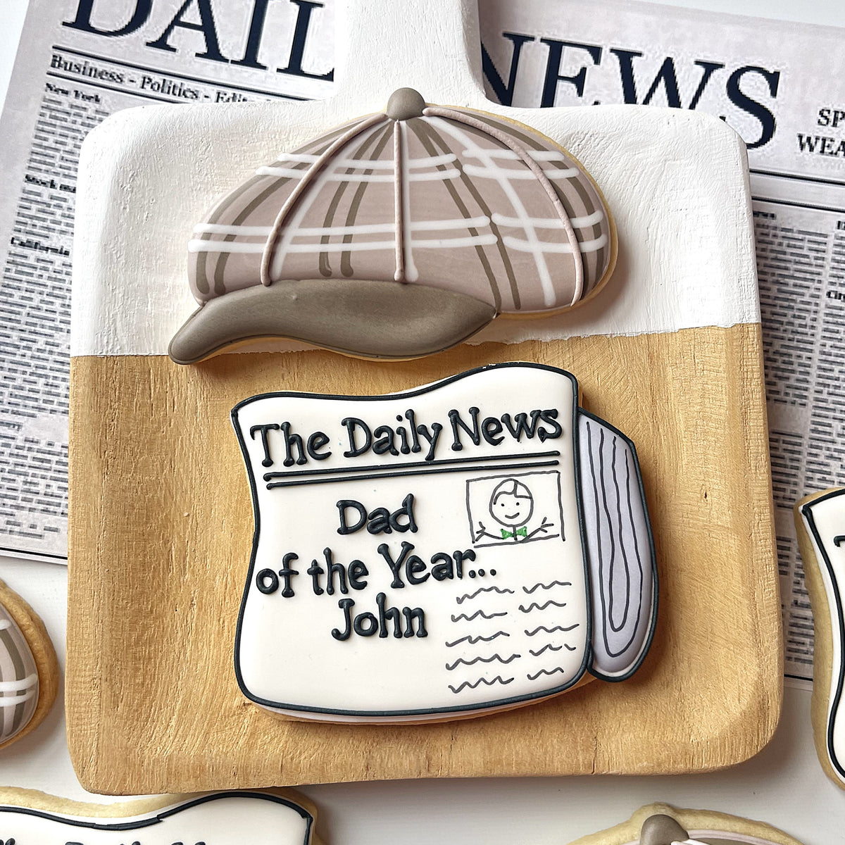 Beige and white plaid detective style cap cookie with glossy finish on newspaper themed cookie from fathers day 2025 set