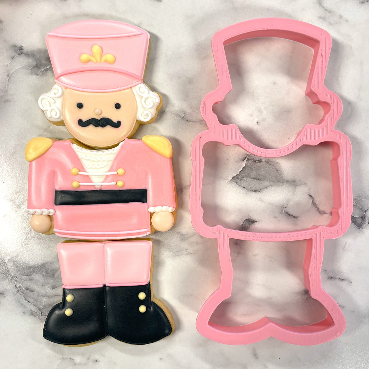 Pink plastic nutcracker 3-in-1 multi-cookie cutter next to a decorated pink and black sugar cookie in the same shape