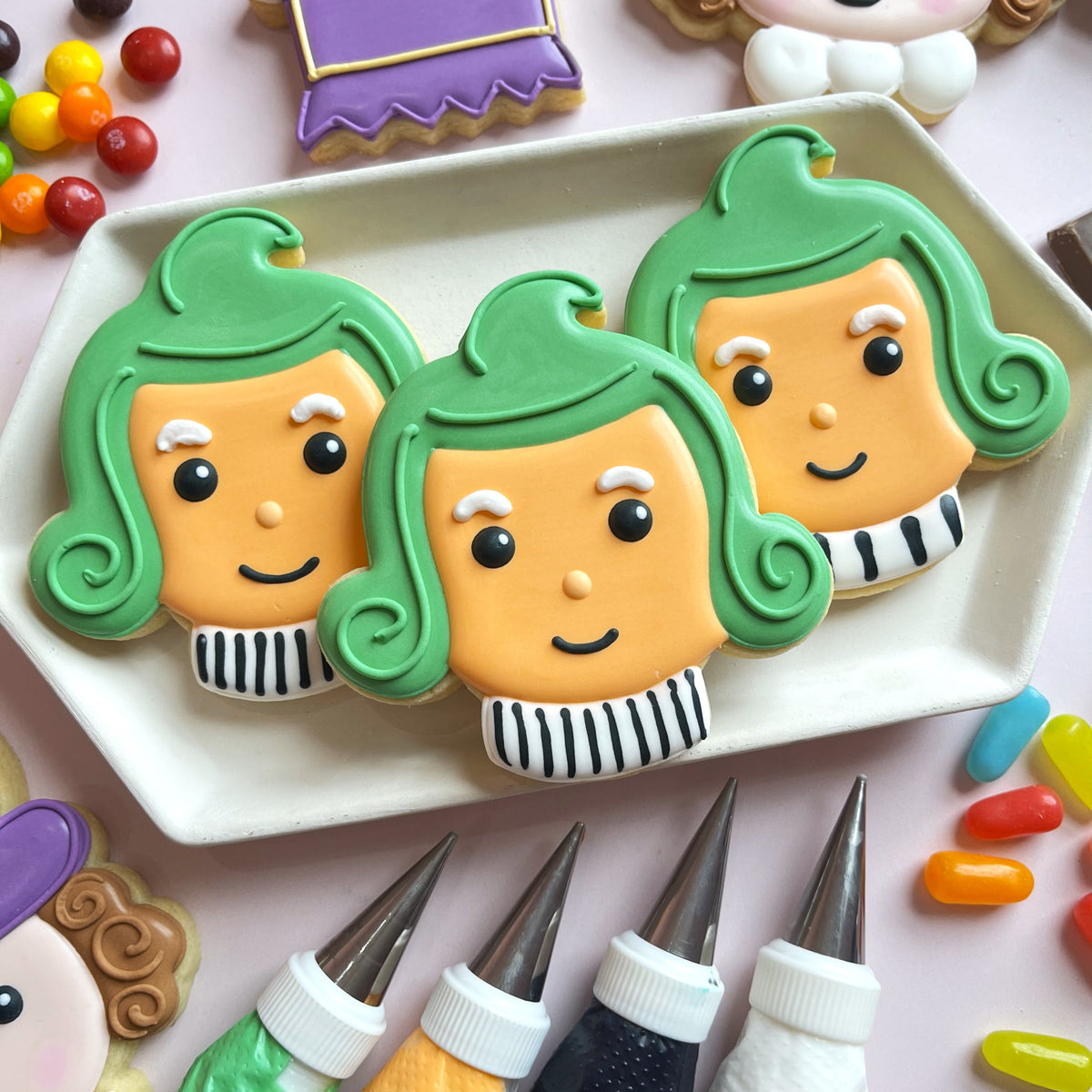 Three intricately decorated green-haired orange-faced sugar cookies with black and white striped collars from candymaker cutter bundle